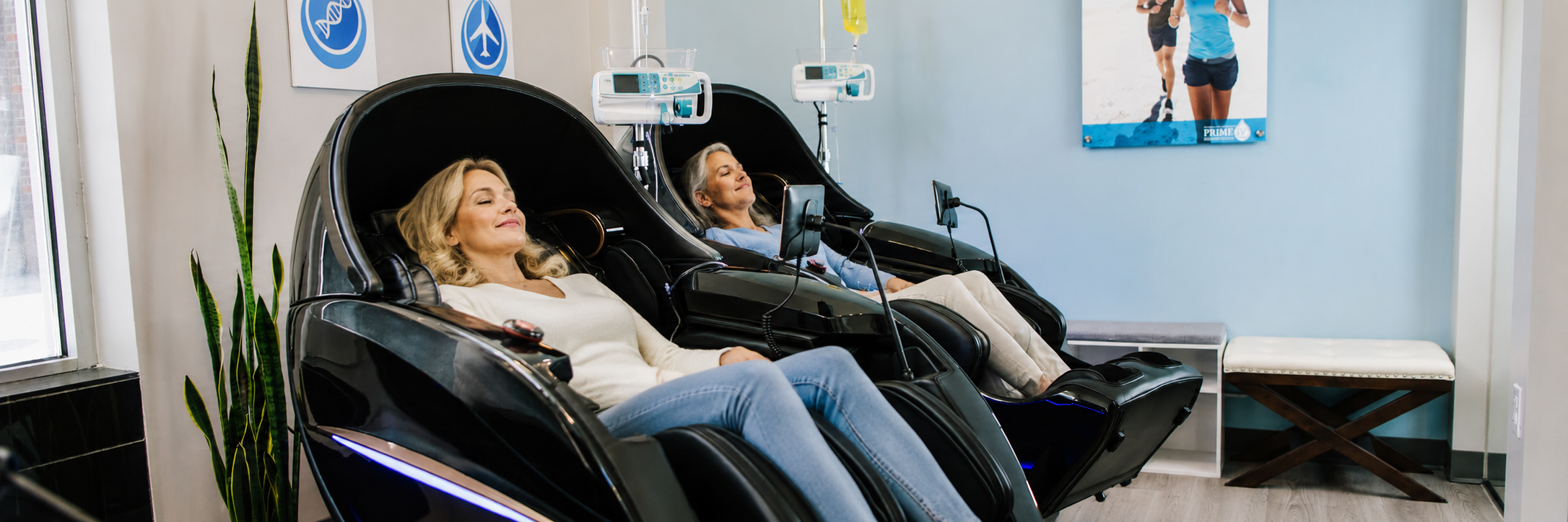 Two women relaxing in zero-gravity massage chairs while receiving IV therapy at Prime IV